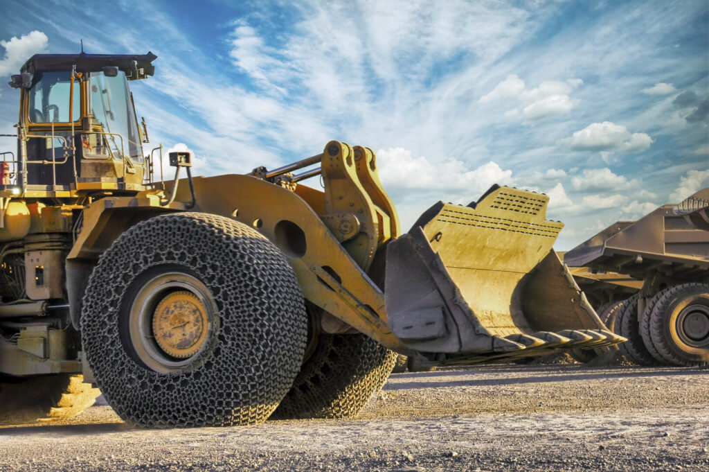 wheel loader at a diamond mine with parked mining trucks, chains on the front wheels to protect tires and for the grip, outdoors sunset with blue sky and sun rays 10 Insights 1024x681