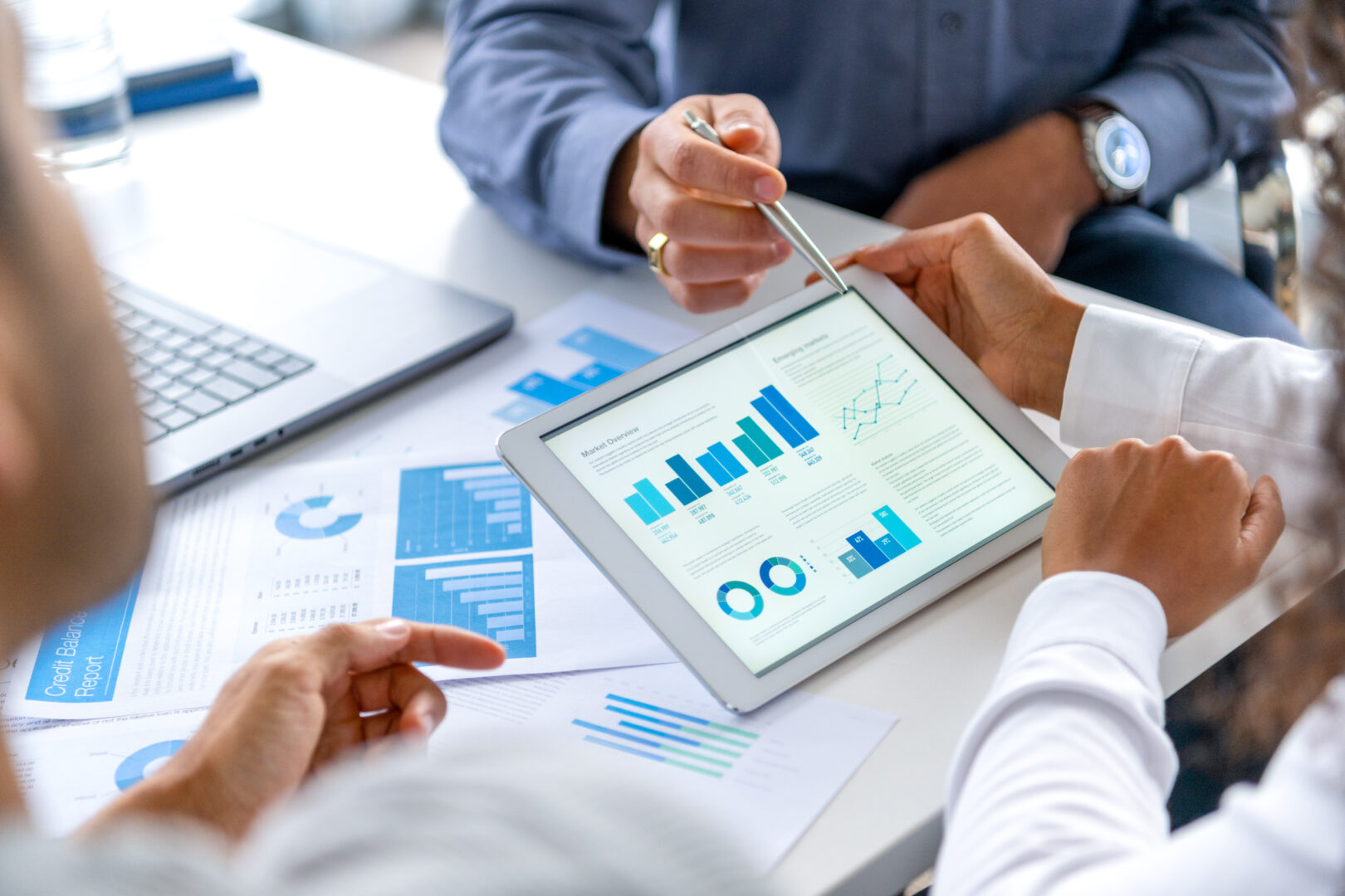 Close up of three people looking at financial data with graphs and charts.