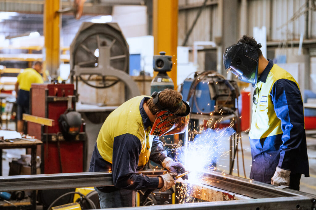 Worker in protective gear welding metal in an industrial factory setting with sparks flying around brightly illuminating the area 9 Insights 1024x683